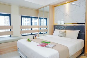 A hotel room with a bed, a bedside table, a window with blinds, a mirror, and a view of buildings outside. - Compact Studio Near President University At Pollux Chadstone Apartment (Cikarang)