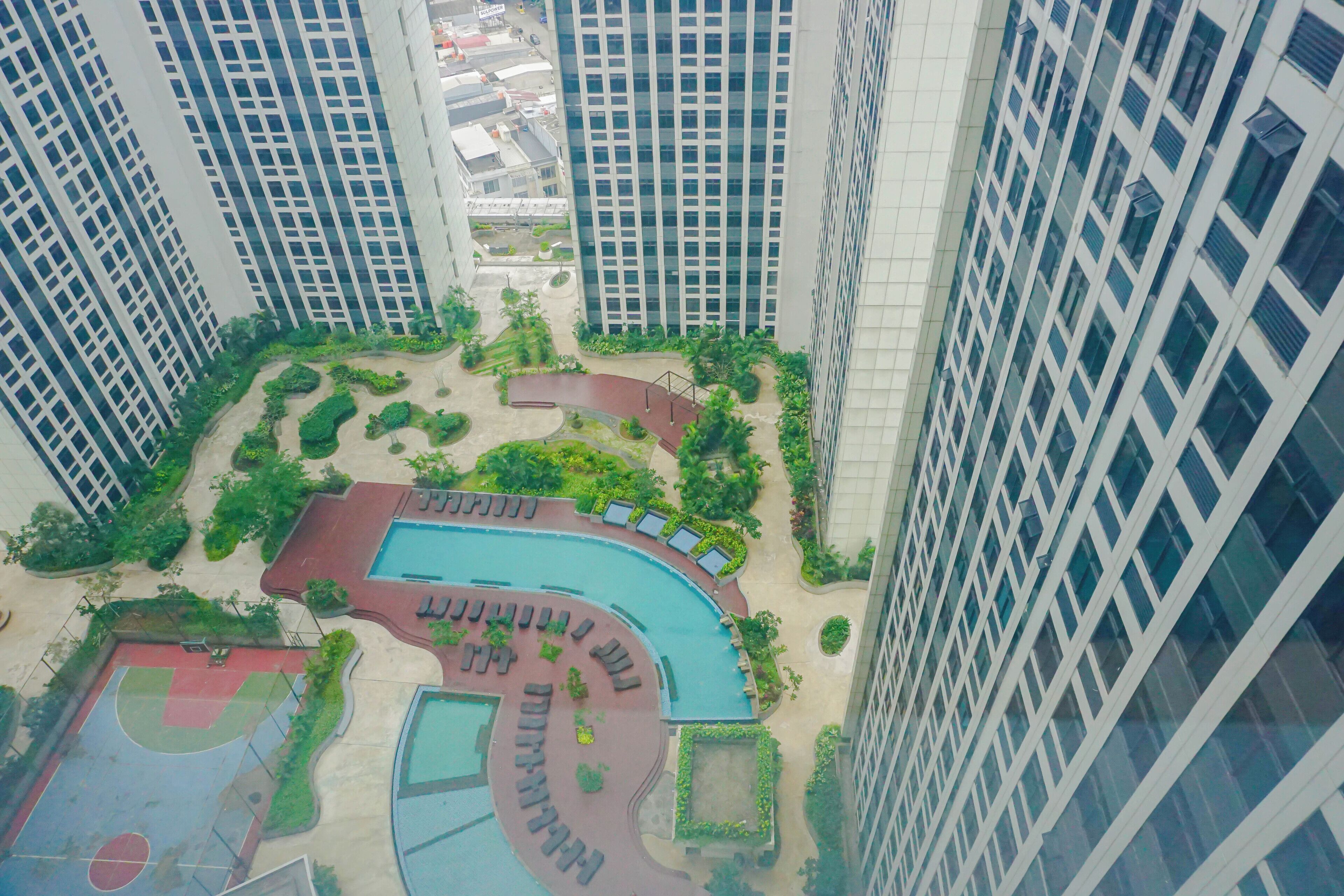 A high-rise building with a rooftop pool surrounded by greenery and a basketball court.