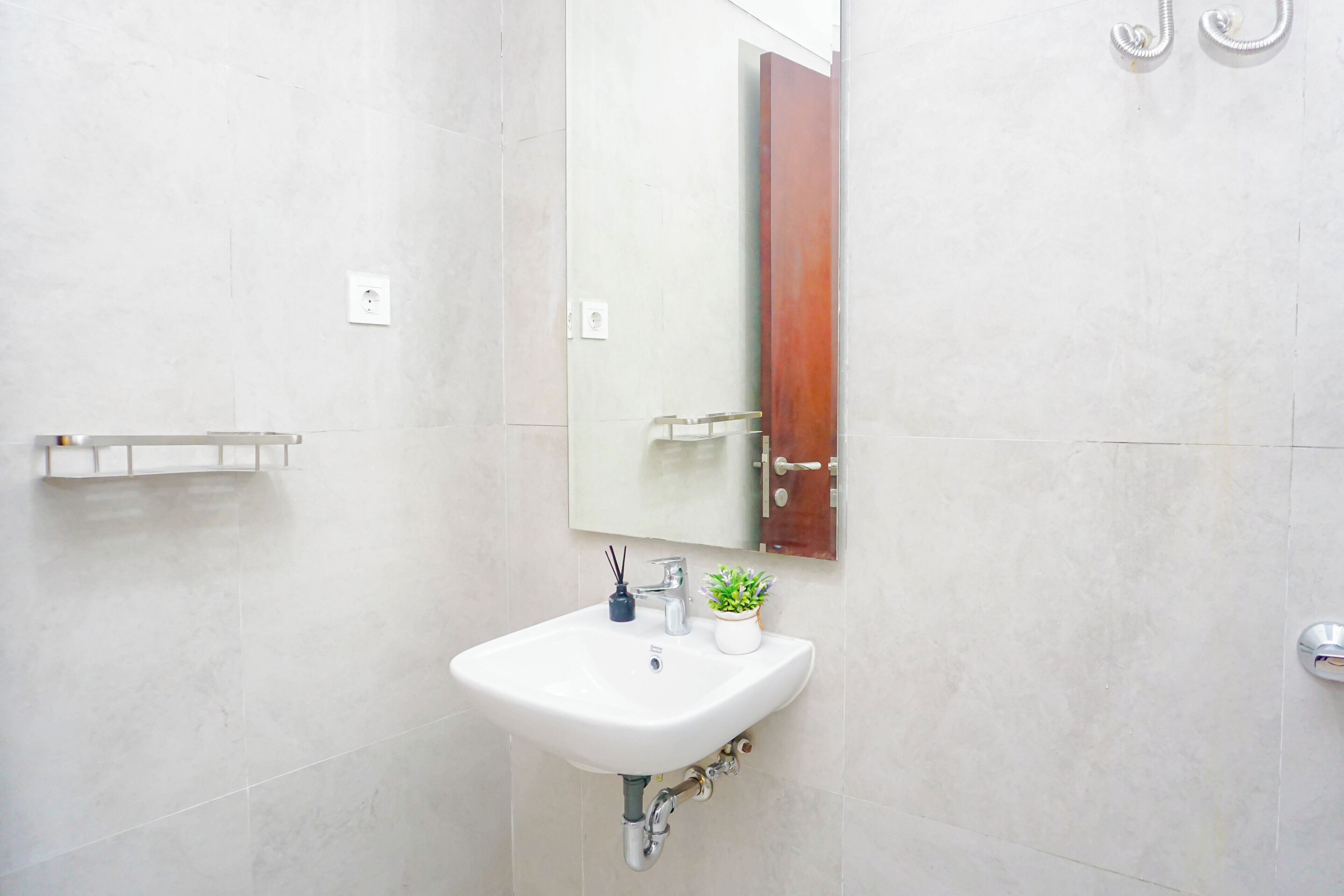 Une salle de bain avec un lavabo blanc, un miroir et une petite plante en pot.