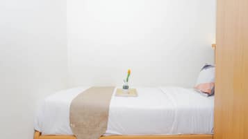 A single bed with a wooden frame, white bedding, a beige throw blanket, and a small bedside table with a vase of flowers.
