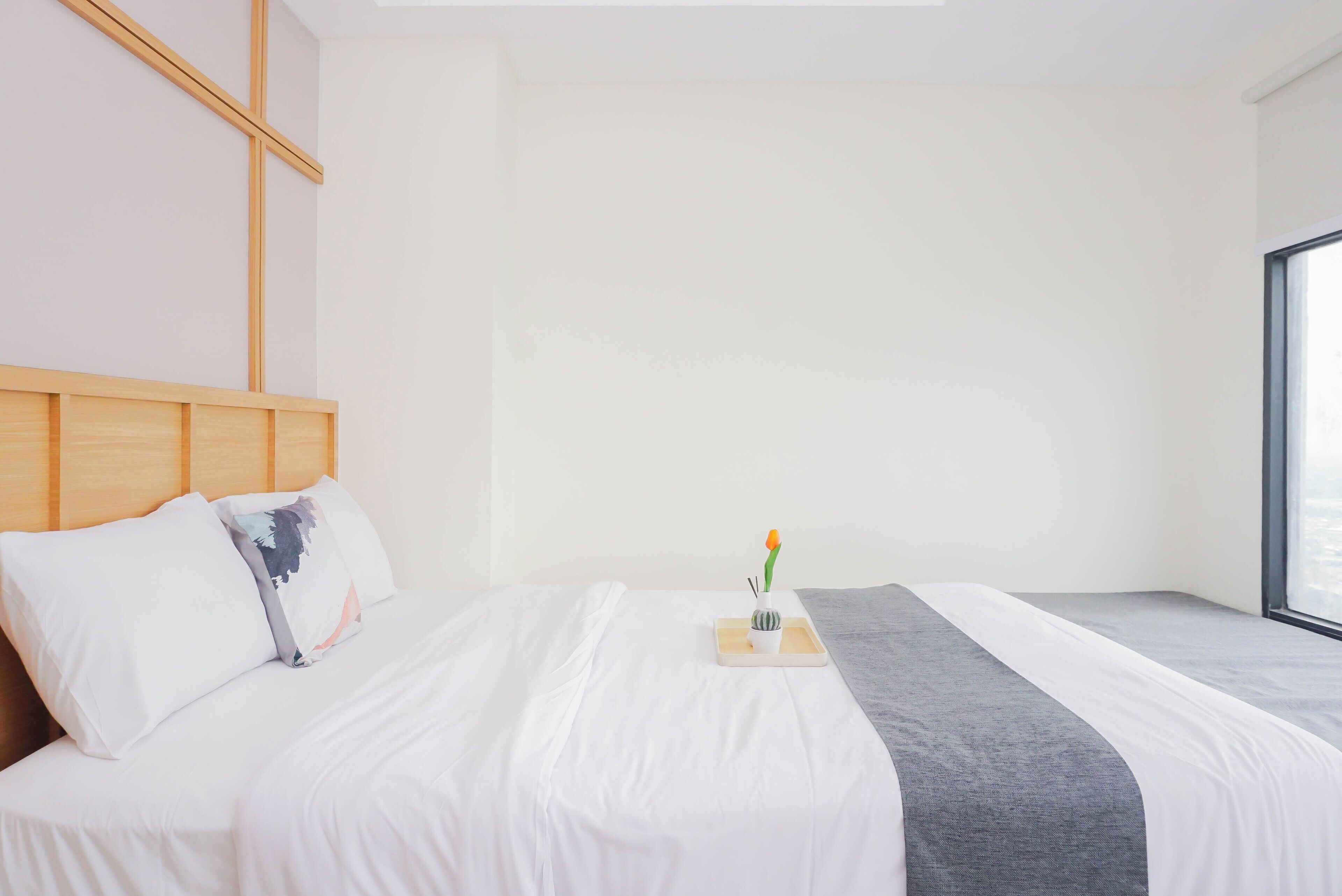 A hotel room with a large bed, a headboard, a bedside table with a vase and a candle, and a window.