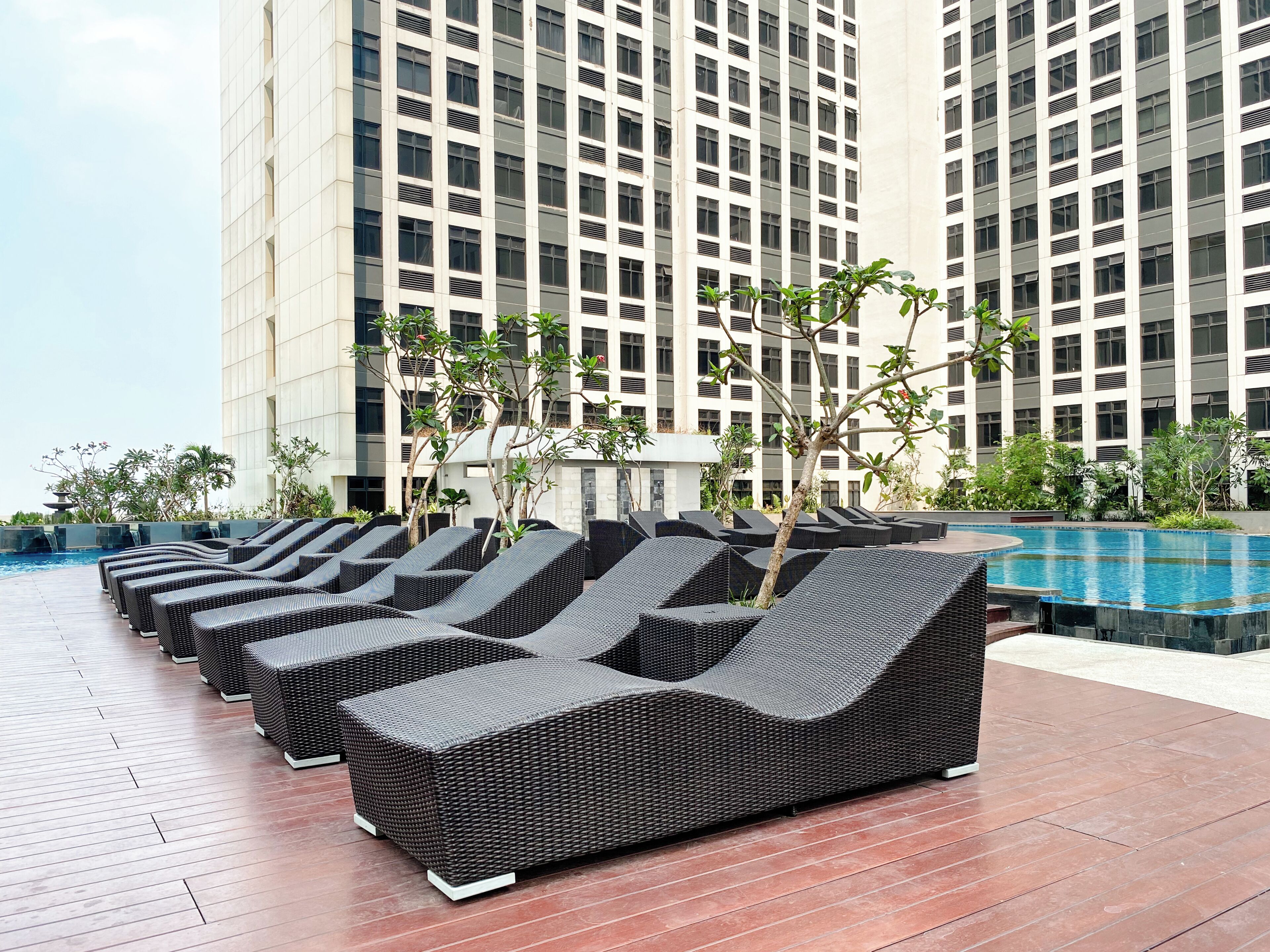 A row of black wicker lounge chairs by a swimming pool with a modern building in the background.