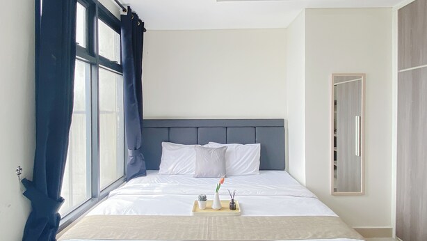 A hotel room with a large bed, a bedside table with a tray, and a window with curtains. - Citylight Studio At Apartment Pollux Chadstone (Cikarang)