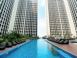 Piscina com espreguiçadeiras e edifícios altos ao fundo.