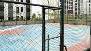 A basketball court enclosed by a chain-link fence with a basketball hoop visible in the background. - Citylight Studio At Apartment Pollux Chadstone (Cikarang)
