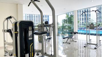 A gym with various exercise machines, a bench, and a view of a swimming pool through large windows.