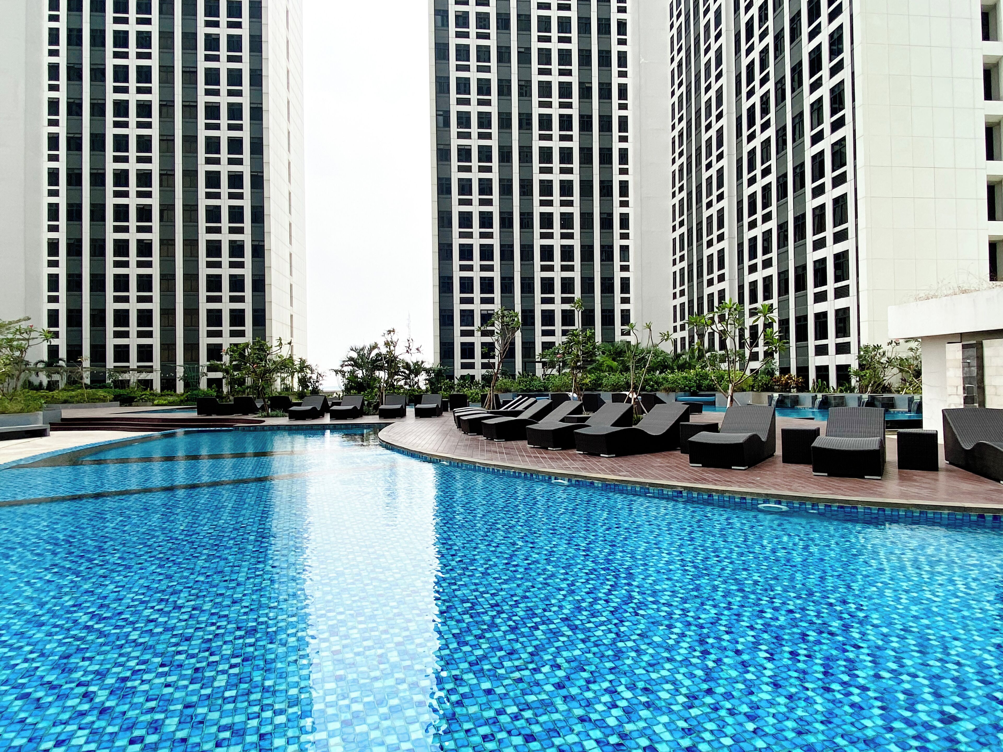 A swimming pool with lounge chairs and tall buildings in the background.
