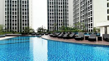 A swimming pool with lounge chairs and tall buildings in the background.