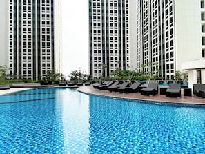A swimming pool with lounge chairs and tall buildings in the background. - Modern Haven Studio At Apartment Pollux Chadstone (Cikarang)