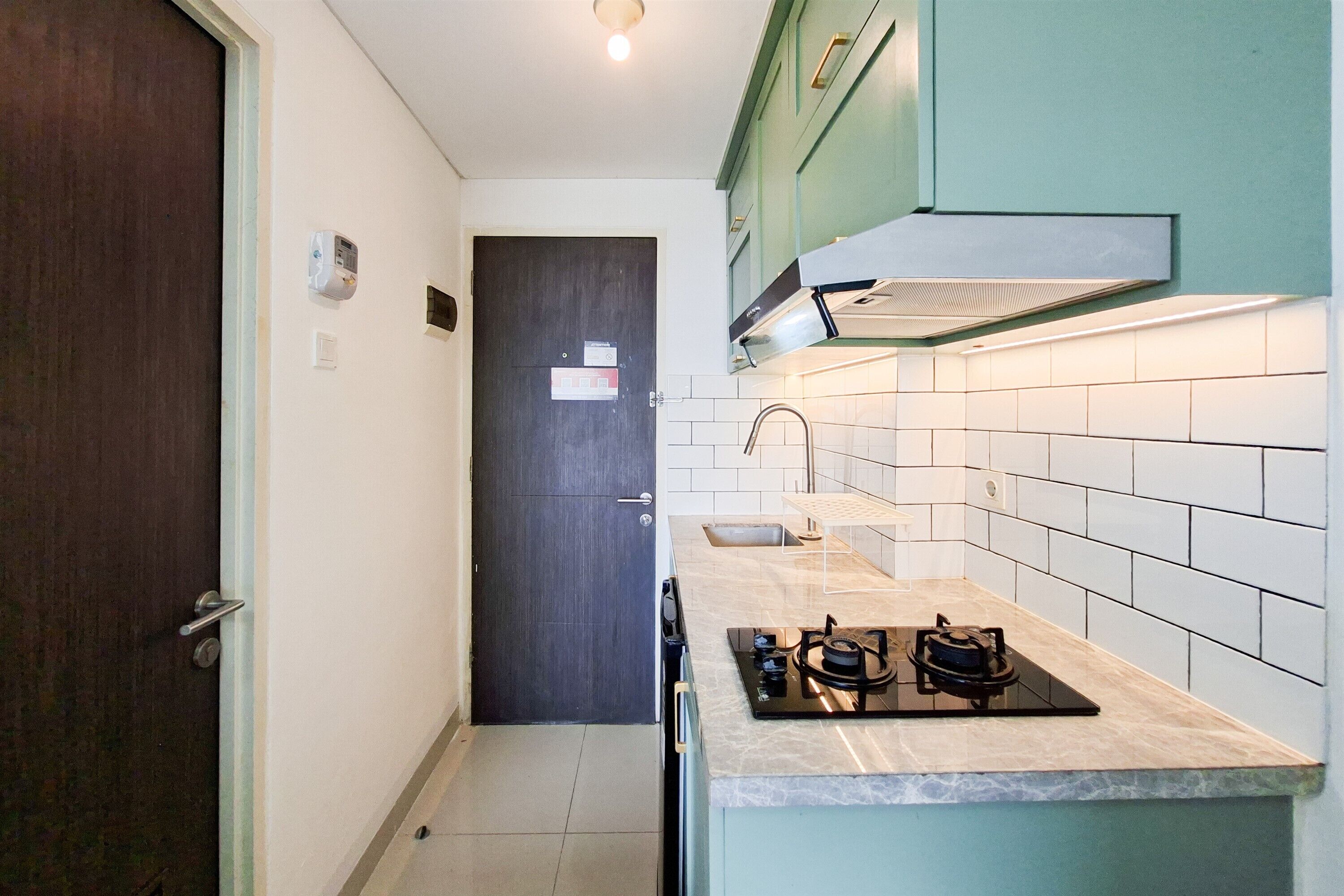 Una cocina compacta con una puerta oscura, salpicadero de azulejos blancos y una estufa a gas.