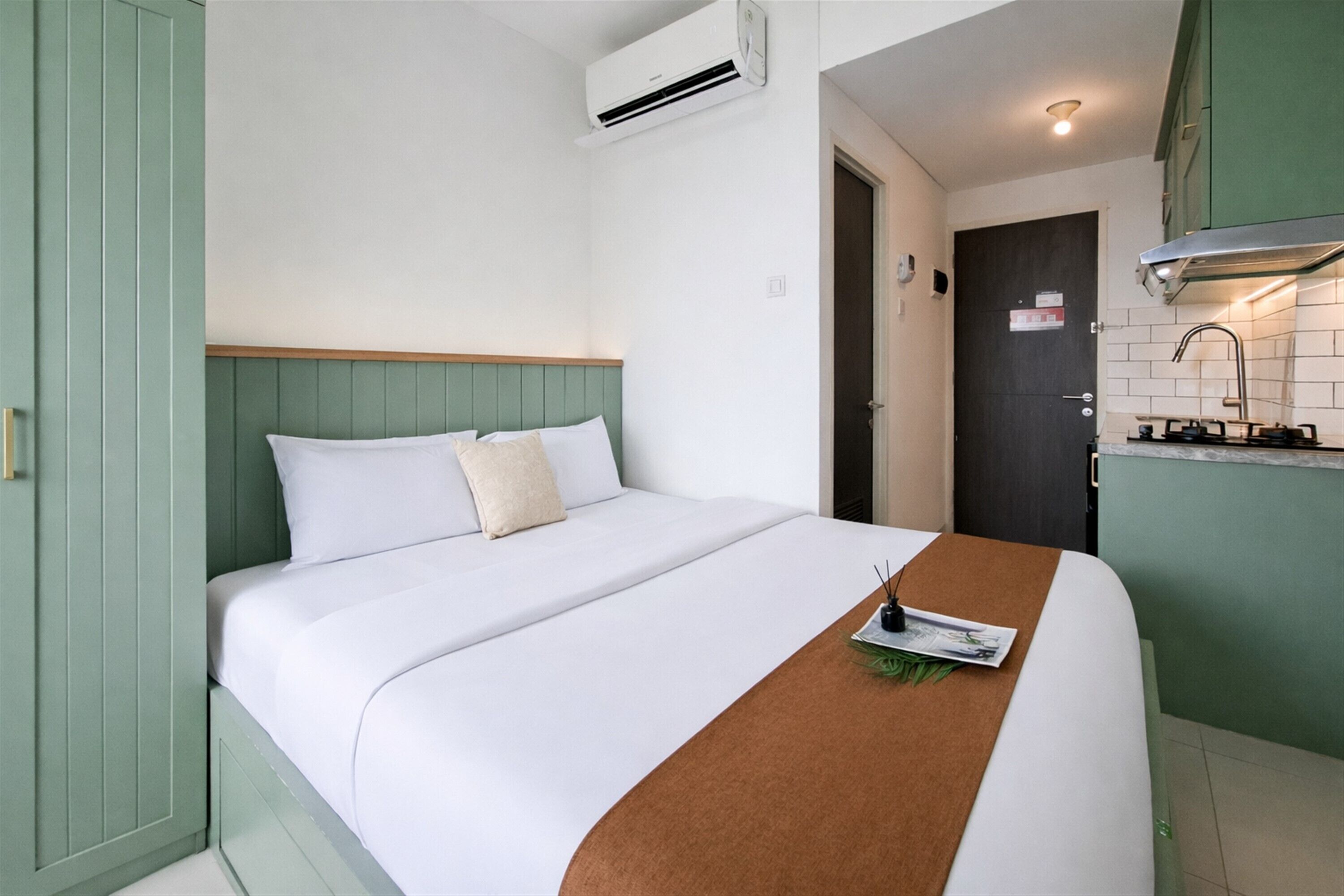 A hotel room with a bed, a kitchenette, and a door leading to another room.