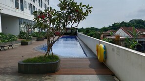 A rooftop pool with a wooden deck, a small tree, and a yellow inflatable ring. - Chic Modern Style Studio Apartment At Serpong Garden (Cisauk)