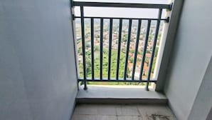A balcony with a metal railing, a concrete floor, and a view of a residential area with houses and greenery. - Comfortable And Modern Studio Room At Serpong Garden Apartment (Cisauk)
