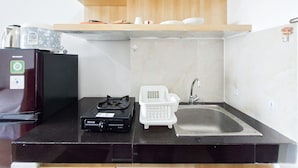 A compact kitchen with a refrigerator, a stove, a sink, and a microwave. - Comfortable And Modern Studio Room At Serpong Garden Apartment (Cisauk)