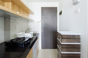 A compact kitchen with a gas stove, a sink, and a door leading to another room. - Comfortable And Modern Studio Room At Serpong Garden Apartment (Cisauk)