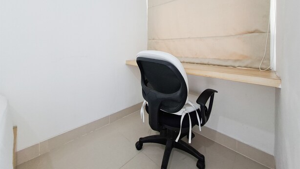 A corner office with a black office chair, a wooden shelf, and a tiled floor. - Comfortable And Modern Studio Room At Serpong Garden Apartment (Cisauk)