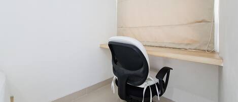 Una oficina en esquina con una silla de oficina negra, un estante de madera y piso de baldosas.