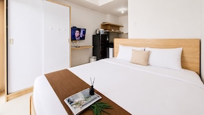 A hotel room with a bed, a television, a wardrobe, and a kitchenette. - Comfortable And Modern Studio Room At Serpong Garden Apartment (Cisauk)