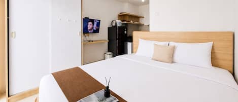 A hotel room with a bed, a television, a wardrobe, and a kitchenette.