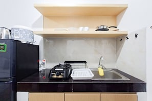 Una cocina compacta con cubierta negra, un lavamanos pequeño, un tostador, un hervidor y una cocedora de arroz.