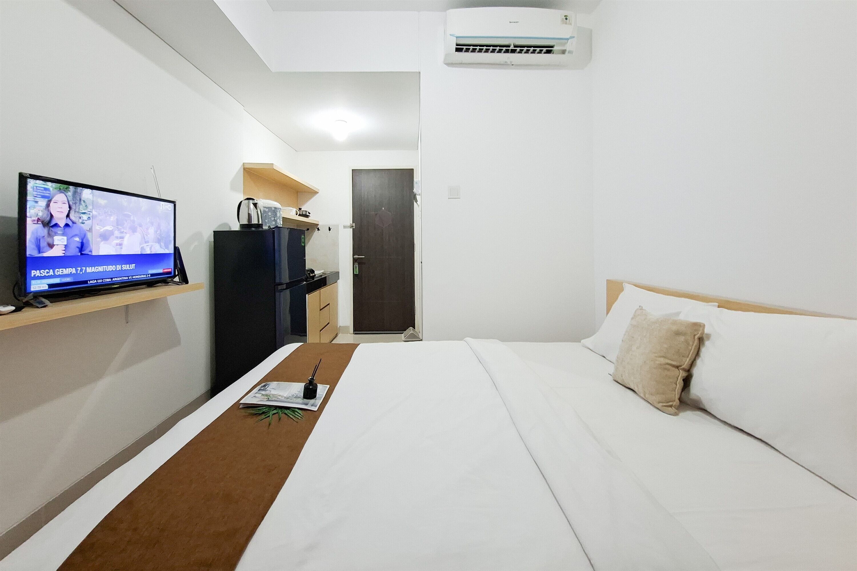 Una habitación de hotel con cama, televisor sobre un mueble bajo, un escritorio pequeño y una puerta.