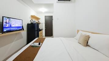 Una habitación de hotel con cama, televisor sobre un mueble bajo, un escritorio pequeño y una puerta.