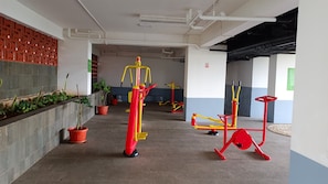 A corridor with exercise equipment, potted plants, and a brick wall. - Comfortable Studio At Apartment Serpong Garden (Tangerang)