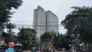 A tall residential building with multiple floors and balconies, surrounded by trees and power lines. - Good Deal Studio (No Kitchen) Apartment Skyland City Jatinangor (Sumedang)