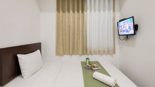 Quarto de hotel com uma cama, televisão fixada na parede e uma janela com cortinas.