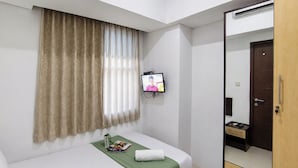 Camera d'albergo con un letto, una televisione a parete, una finestra con tende e un armadio.