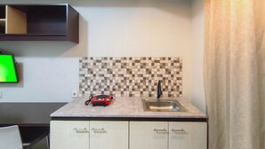 A kitchen with a tiled backsplash, a sink, and a countertop. - Comfy Studio Apartment Skyland City Jatinangor (Sumedang)