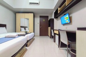 Quarto de hotel com duas camas, uma escrivaninha, uma cadeira, uma televisão e uma porta.