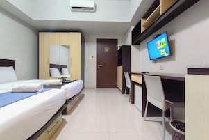 Habitación de hotel con dos camas, un escritorio, una silla, un televisor y una puerta.