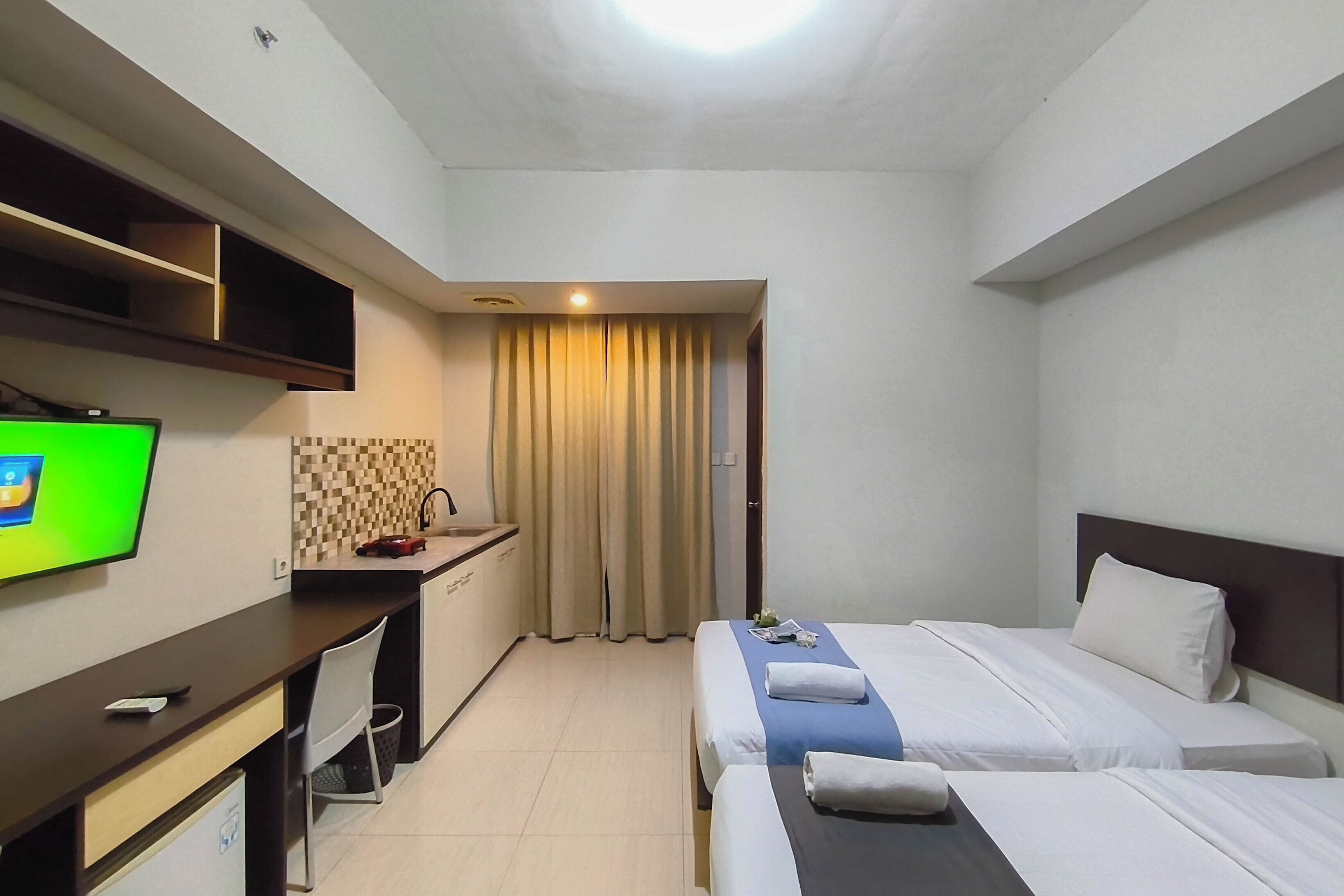 Una habitación de hotel con cama, escritorio con televisor y kitchenette.