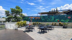An outdoor patio with tables and chairs, a mural on the wall, and a clear blue sky. - Comfy Studio Apartment Skyland City Jatinangor (Sumedang)