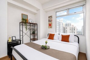 A modern bedroom with a bed, a window with a city view, a shelf with plants, and a clock on the wall. - Restful And Serene Studio Room At Apartment Green Bay Pluit (Jakarta)