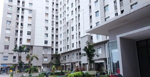 Un edificio residencial de varios pisos con balcones, una planta baja comercial y un patio ajardinado.