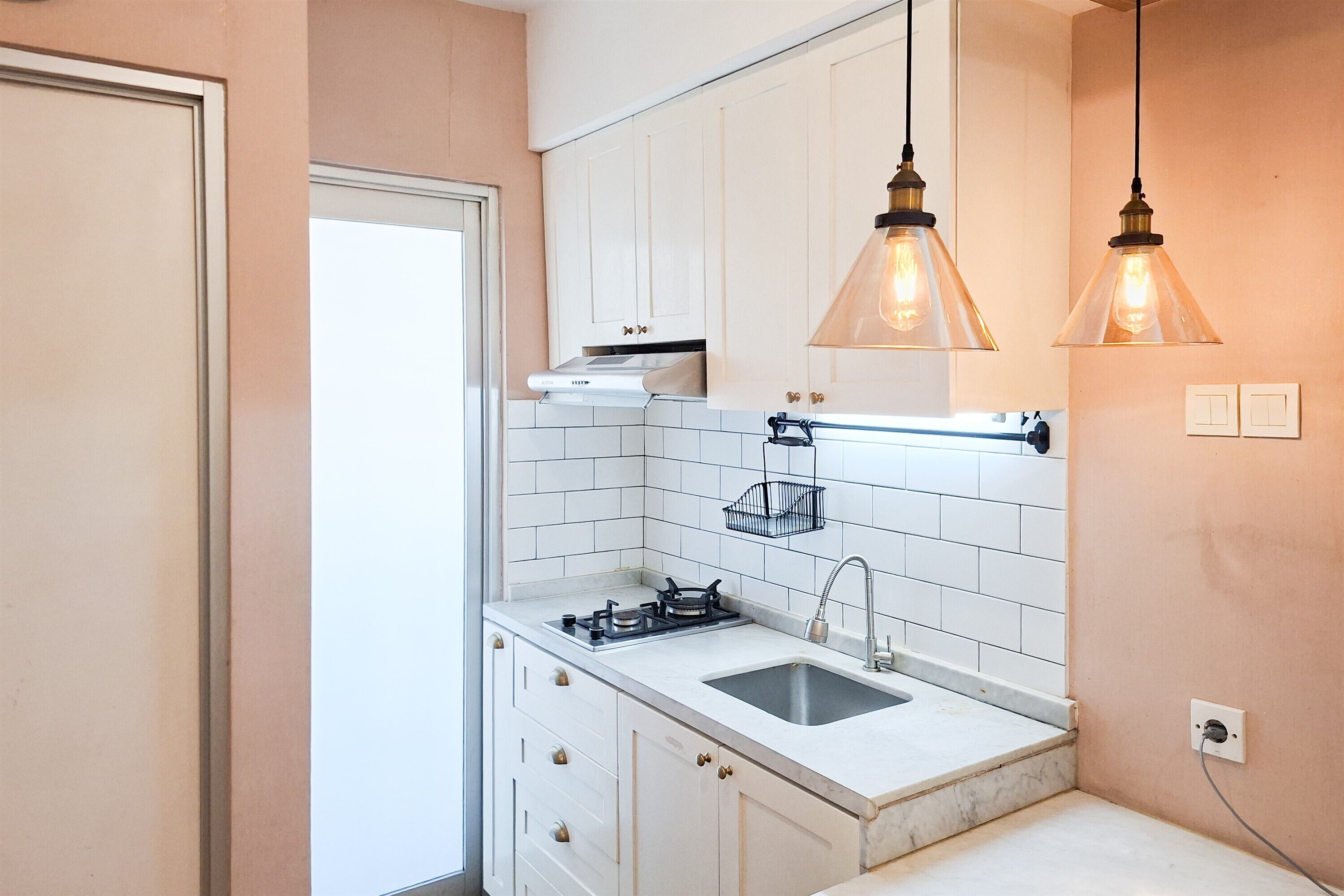 Cocina con armarios blancos, pileta de acero inoxidable e iluminación colgante.