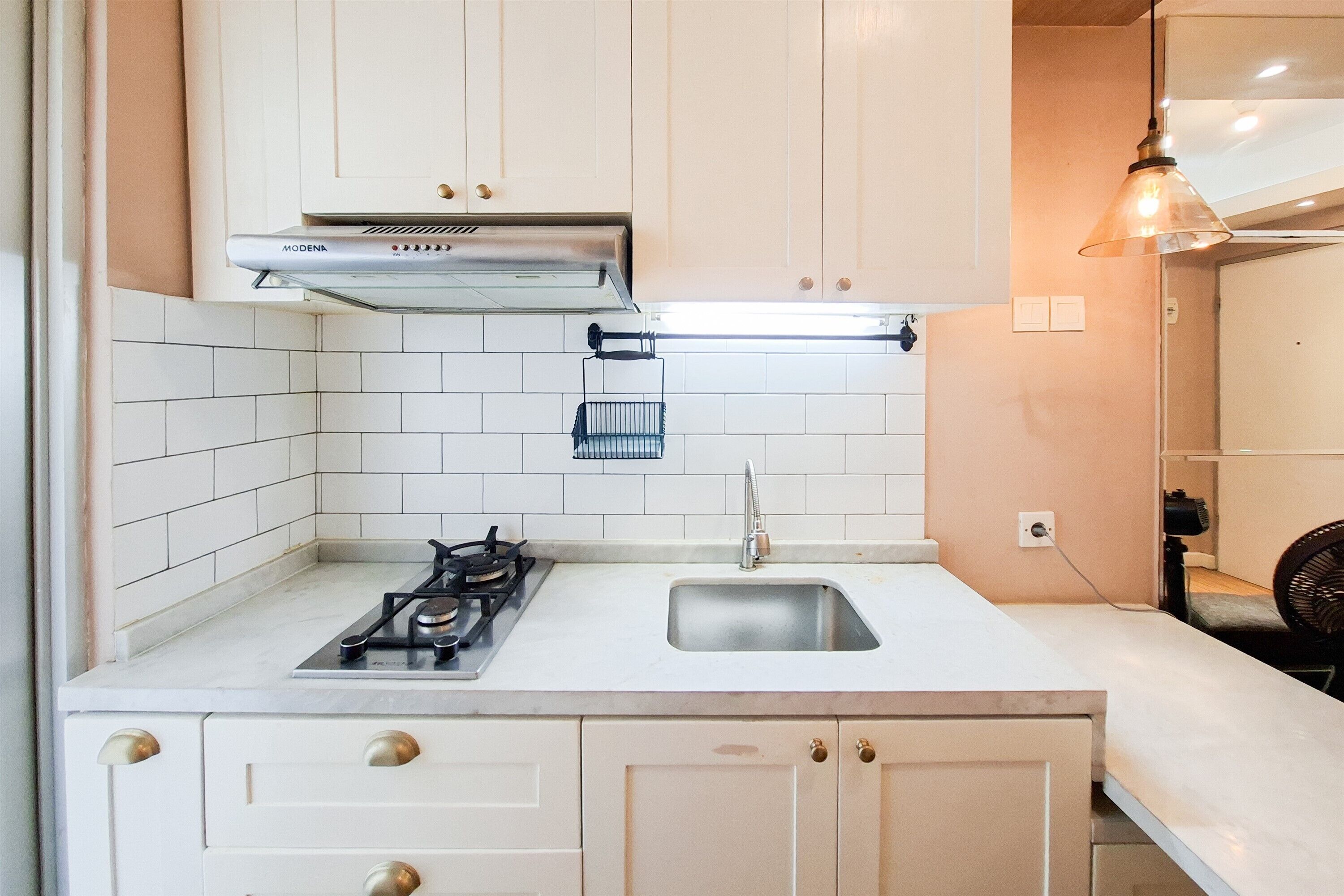 A compact kitchen with white cabinets, a gas stove, a stainless steel sink, and a range hood.