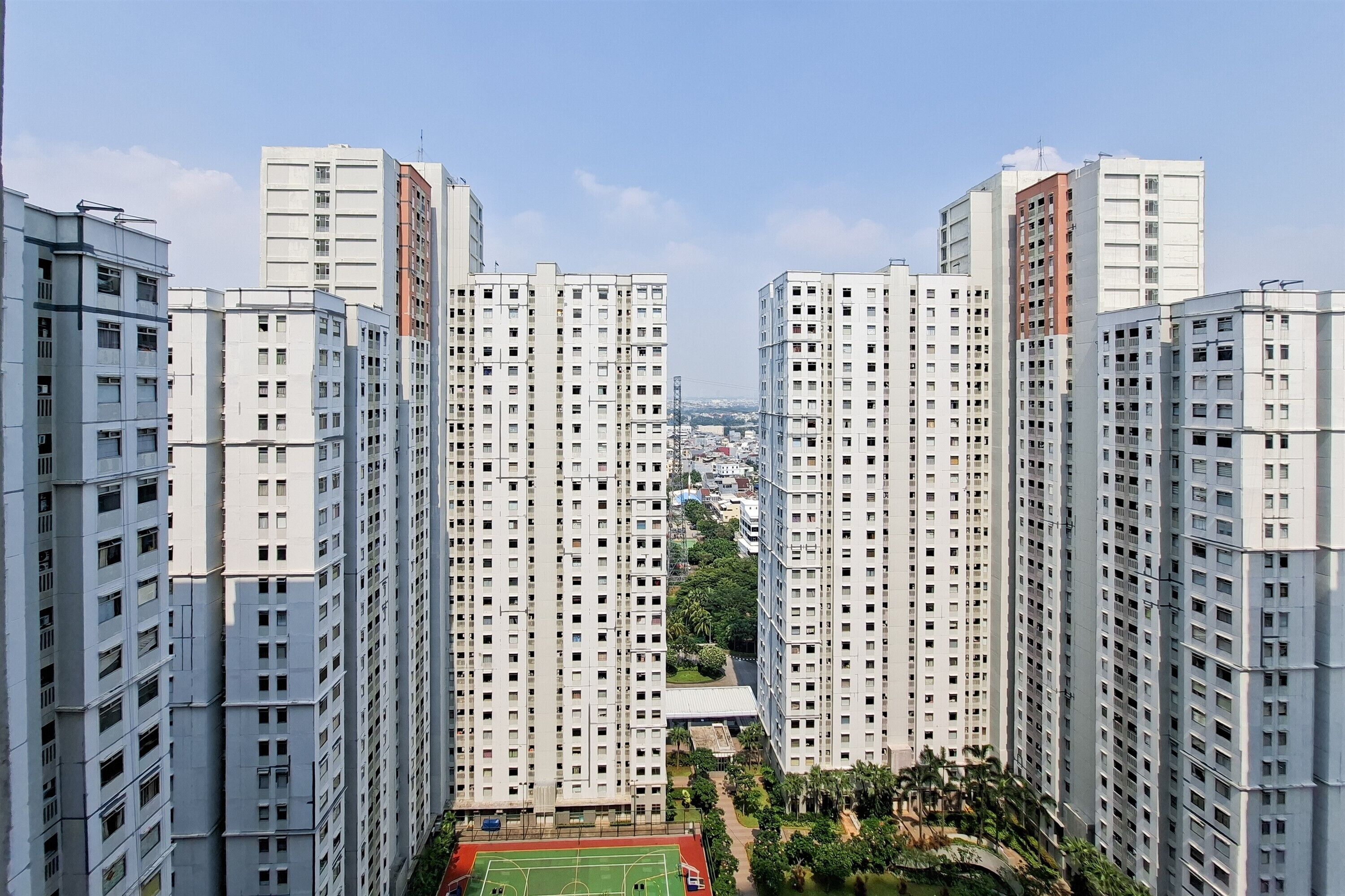 Un edificio residencial de gran altura con varios pisos, un patio central con vegetación y una vista despejada del paisaje urbano circundante.