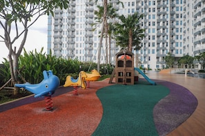 A children's play area with colorful equipment, a slide, and a small treehouse structure. - Cityscape Studio At Apartment Benson Supermall Mansion (Surabaya)