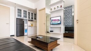 A modern living room with a glass coffee table, a sofa, and a TV mounted on the wall. - Serene Spacious 2Br At Apartment Benson Supermall Mansion (Surabaya)