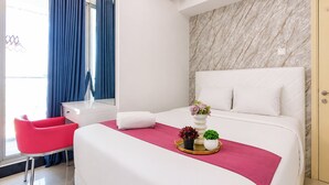 A hotel room with a bed, a desk, a chair, and a window with curtains. - Serene Spacious 2Br At Apartment Benson Supermall Mansion (Surabaya)