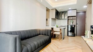 Una sala de estar moderna con un sofá gris, piso de madera en espiga y una zona de cocina con armarios y un refrigerador.