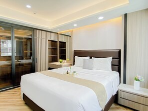 A hotel room with a large bed, a bedside table, a nightstand, a mirror, a wardrobe, and a sliding glass door leading to a balcony. - Serene Wooden Touch 1Br At Apartemen Daan Mogot City (Jakarta)