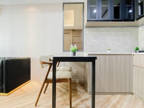 A modern kitchen with a black countertop, wooden chairs, and a built-in sink. - Serene Wooden Touch 1Br At Apartemen Daan Mogot City (Jakarta)