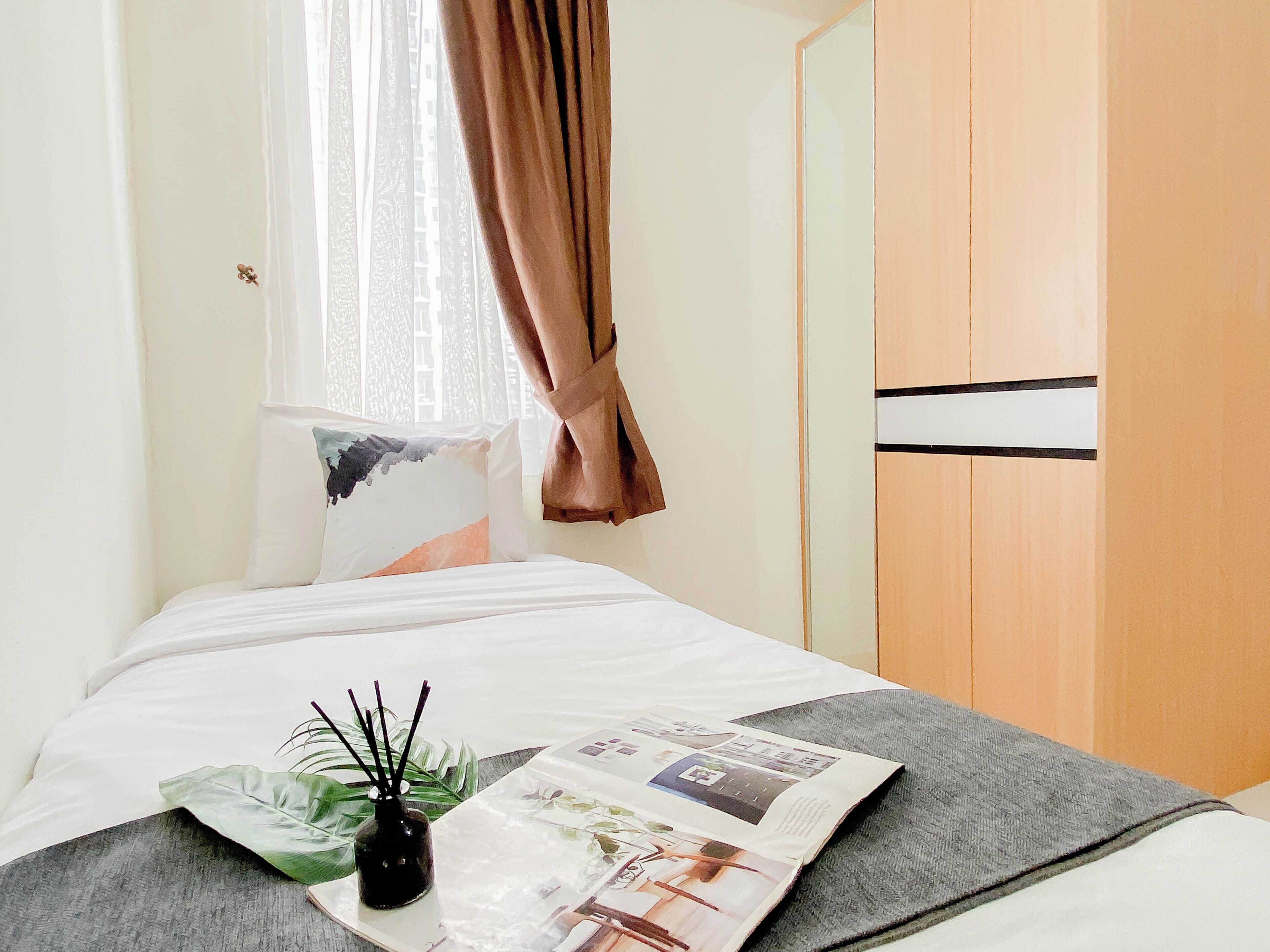 Una cama bien hecha con una revista, una planta pequeña y un florero con ramas.