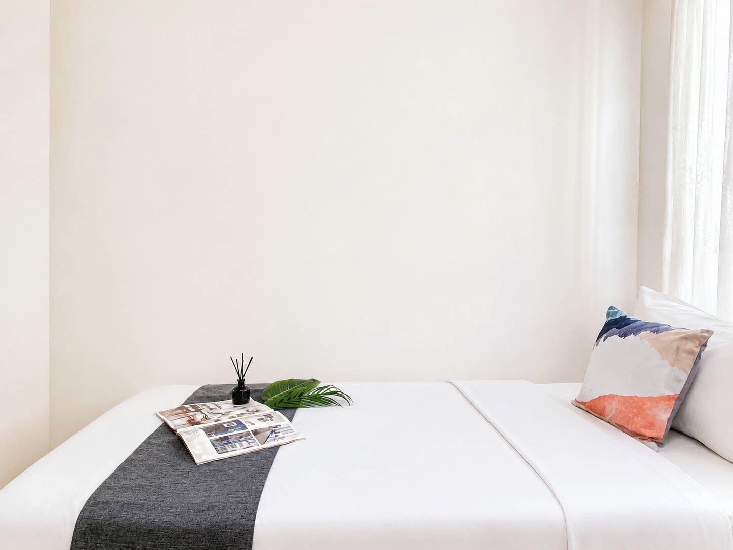 A neatly made bed with a white comforter, a grey throw blanket, and a single decorative pillow.