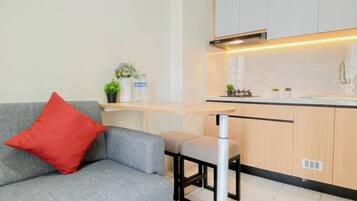 A modern kitchen with a grey sofa, a red pillow, and a small table with decorative items.