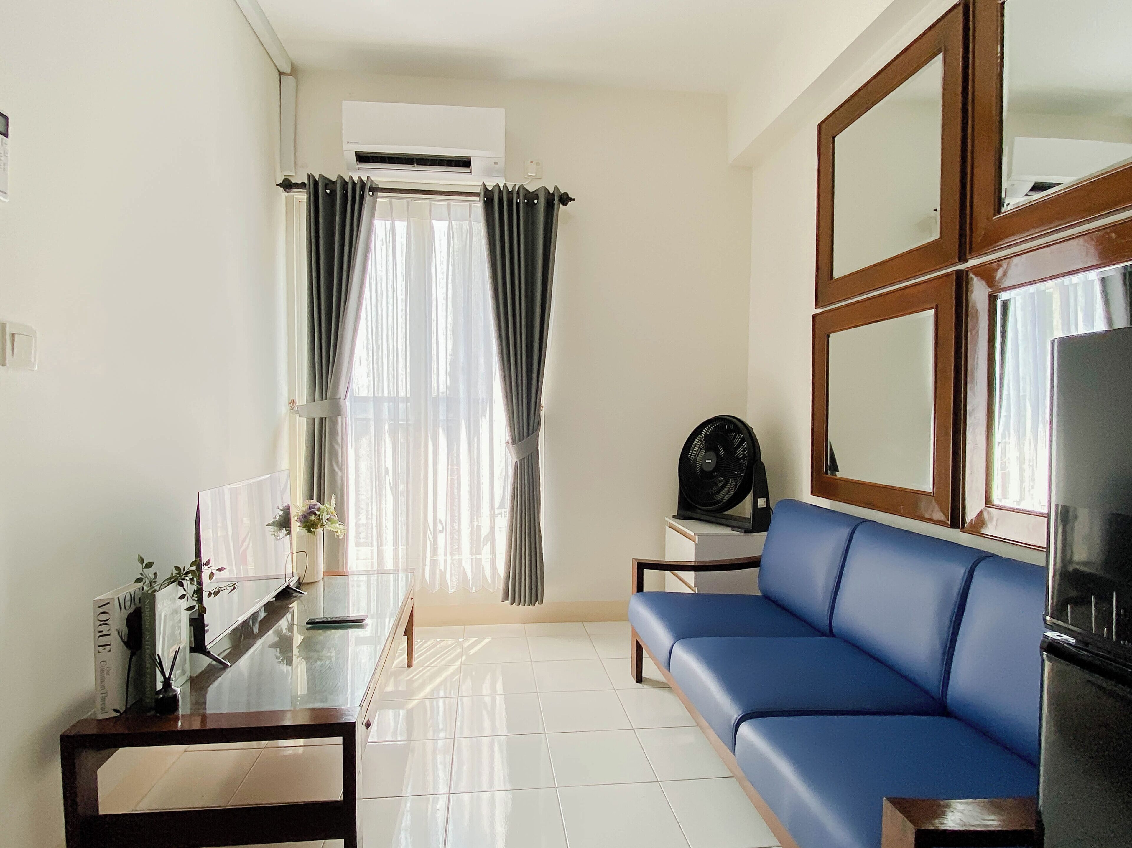 A living room with a blue sofa, a glass coffee table, a small side table, a black fan, and a large mirror.